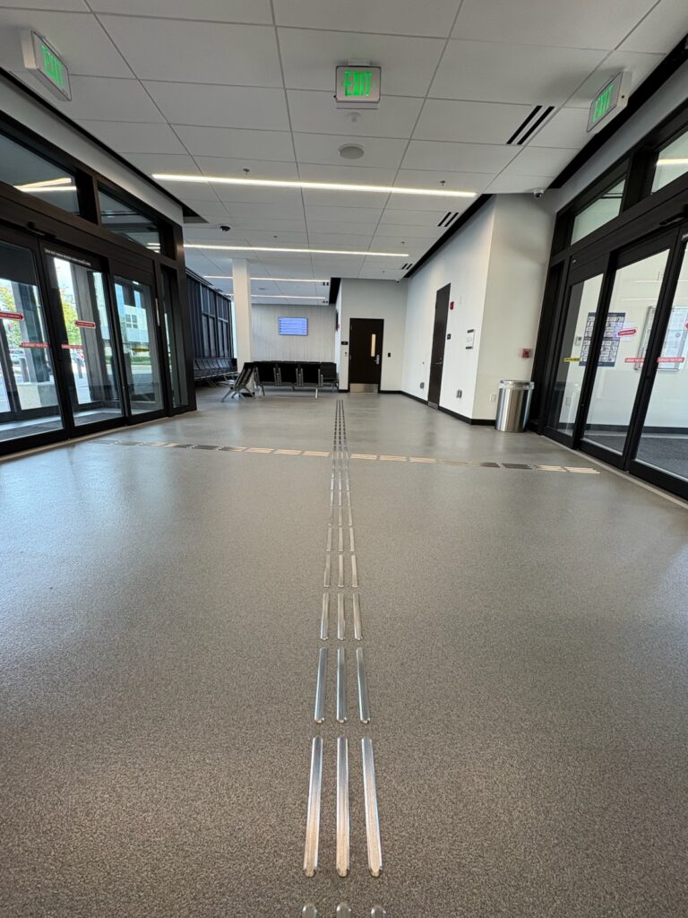 Photo shows a waiting room lobby with seating, entrance doors and tactile guide strips.